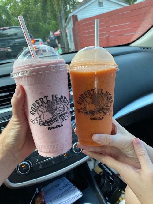 Two hands holding smoothies in branded cups, one pink and one orange, inside a car.