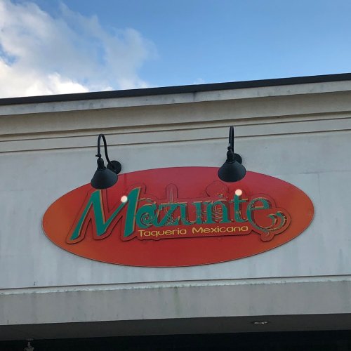 Sign for "Mazunte Taqueria Mexicano" with a colorful design, displayed against a blue sky.