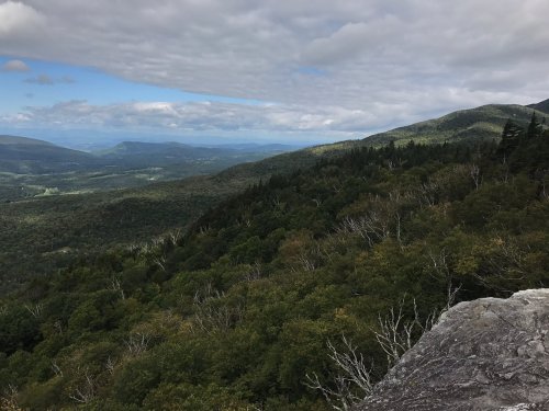 A panoramic view of lush green mountains under a cloudy sky, with valleys stretching into the distance.