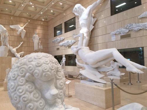 A spacious gallery featuring various white sculptures, including a large sheep and dynamic human figures in motion.