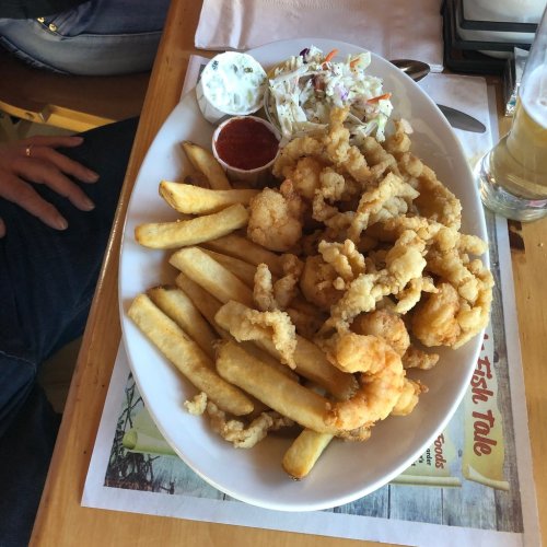 A large plate of fried shrimp and calamari served with French fries, coleslaw, and dipping sauces.