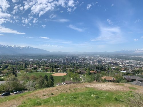 A panoramic view of a city skyline surrounded by green hills and mountains under a clear blue sky.