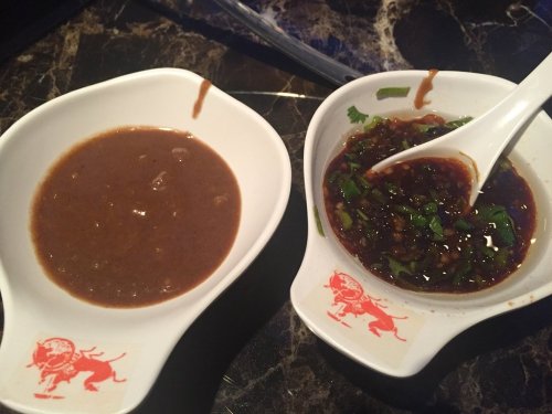 Two small white bowls on a marble surface, one with a brown sauce and the other with a dark sauce topped with green herbs.