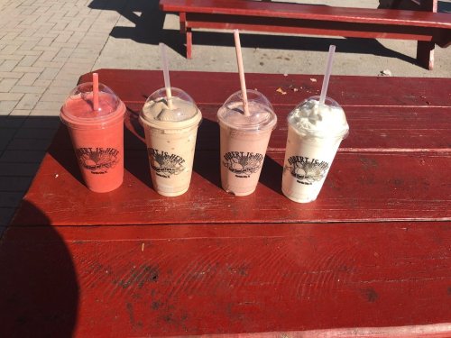 Four colorful smoothie cups with straws sit on a red picnic table in bright sunlight.