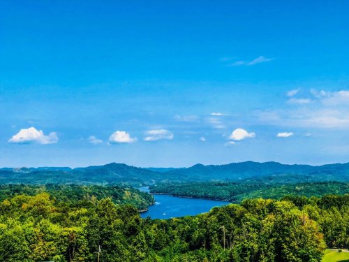 A scenic view of a river winding through lush green hills under a bright blue sky with fluffy white clouds.