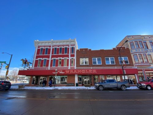 A historic building with red and white accents, featuring "The Wrangler" sign, on a sunny winter day.