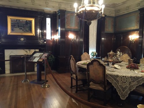 Elegant dining room with a wooden table set, ornate chandelier, and vintage decor, featuring a fireplace and artwork.
