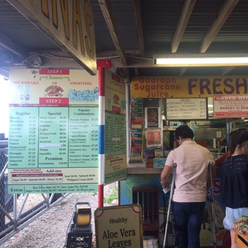 A colorful menu board at a juice stand with customers ordering drinks in a casual outdoor setting.