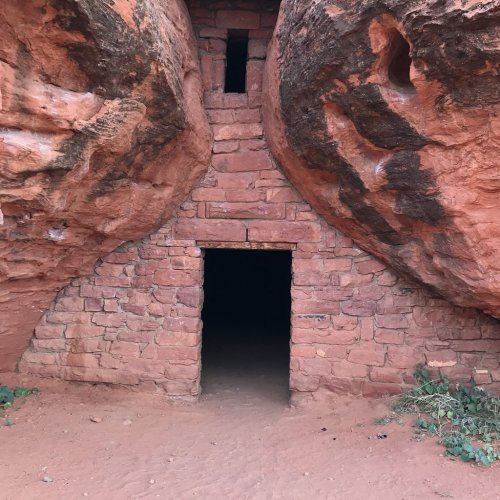 Ancient stone structure nestled between two large rock formations, with a dark entrance and small window above.