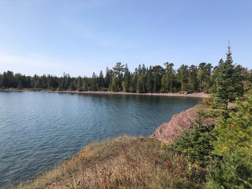 A serene lakeside view with trees lining the shore and a clear blue sky above.