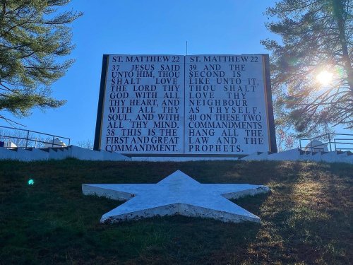 A large sign displaying a Bible verse from St. Matthew 22, set against a backdrop of trees and a white star on the ground.