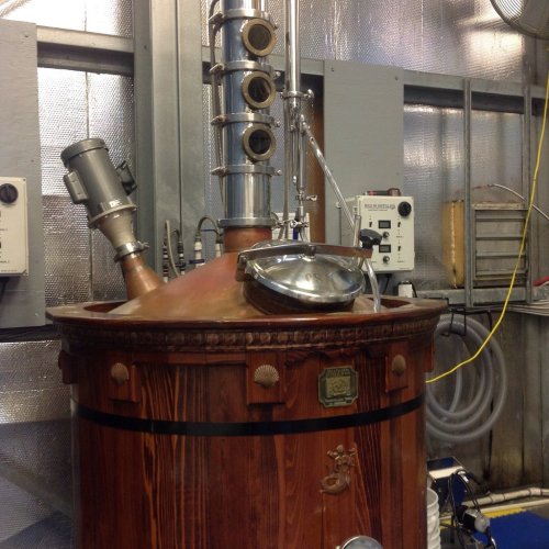 A large copper and wood distillation still with pipes and gauges in a metallic room.