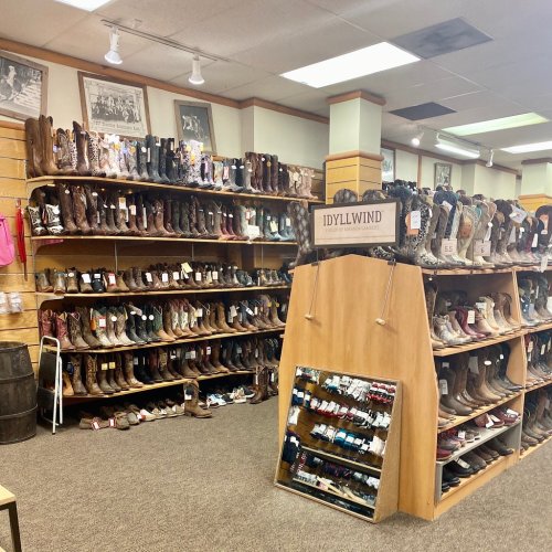 A store interior showcasing a large display of various cowboy boots on shelves and a mirror in the center.