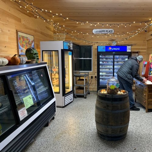 A cozy store interior with refrigerators, a barrel table, and festive lights, featuring snacks and drinks.
