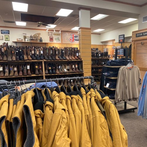 A retail store interior featuring racks of clothing and shelves of boots, with warm lighting and wooden accents.