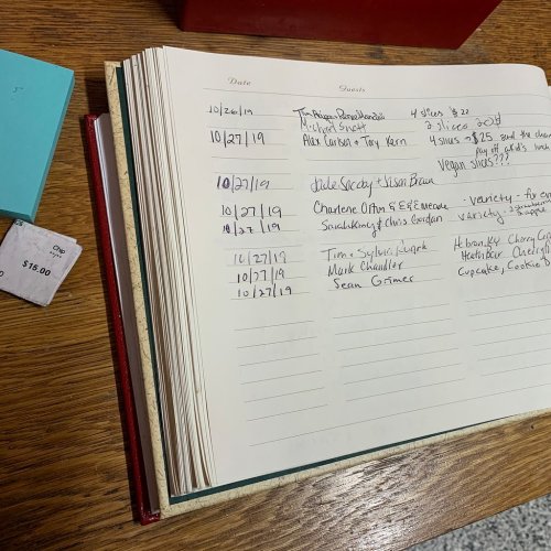 A notebook page with handwritten entries and a small receipt on a wooden table.