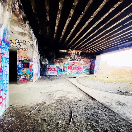 Graffiti-covered walls inside a dark, abandoned structure with exposed beams and a dirt floor.