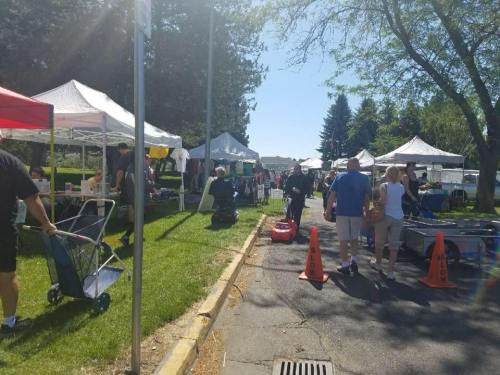 A bustling outdoor market with tents, vendors, and people walking along a sunny path lined with cones.