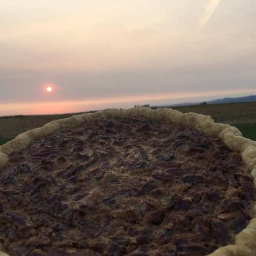 A pecan pie in the foreground with a sunset and distant landscape in the background.