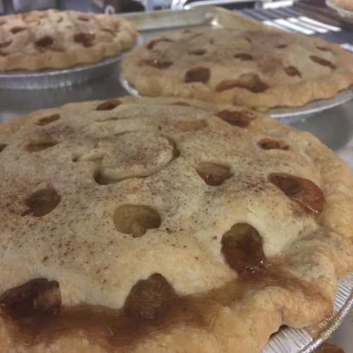 Three freshly baked apple pies with golden crusts and cinnamon topping, cooling on a baking tray.