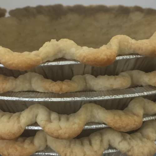 A stack of three uncooked pie crusts in aluminum pans, showcasing their fluted edges.