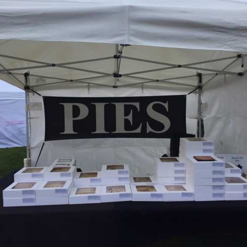 A tent display featuring stacked boxes of pies with a large sign that reads "PIES" in bold letters.