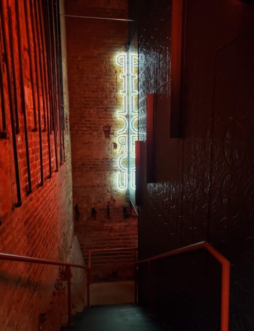 A dimly lit staircase with a glowing neon sign reading "CIRCUS" on the wall, surrounded by textured brick.