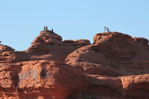 People standing on rocky red formations against a clear blue sky.
