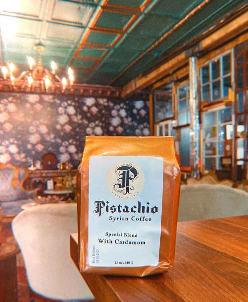 A bag of Pistachio Syrian Coffee with cardamom sits on a wooden table in a cozy, vintage-style room.