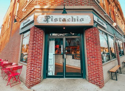 A brick storefront with the sign "Pistachio," featuring outdoor seating and large windows on a sunny day.