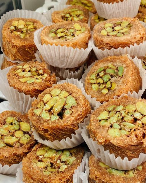A close-up of sweet pastries filled with pistachios, arranged in white paper cups.