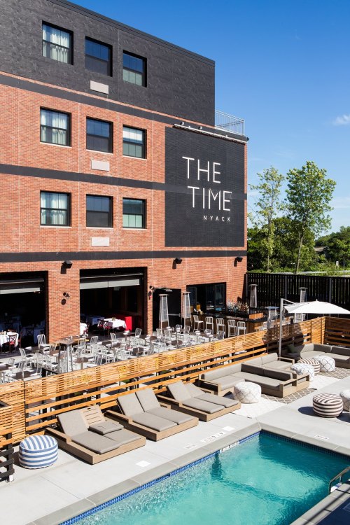 A modern hotel with a pool and lounge area, featuring outdoor seating and a large sign that reads "THE TIME NYACK."