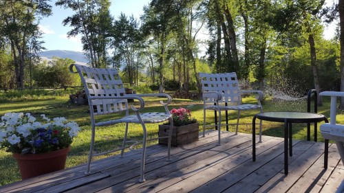 A peaceful outdoor scene with two chairs, a small table, and colorful flowers surrounded by trees and greenery.