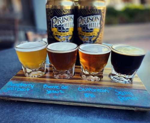 A wooden flight board with four beer samples labeled Raspberry Jailbait, Bierre de Jesus, Outbreak IPA, and Jolly Porter.