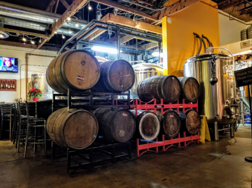 A brewery interior featuring stacked wooden barrels and brewing equipment under warm lighting.