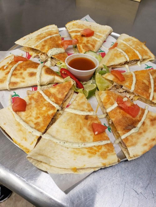 A platter of sliced quesadillas with toppings, served with a small bowl of sauce and lime wedges.