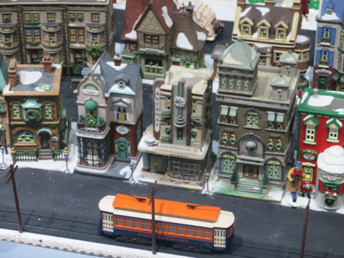 A miniature winter village scene with snow-covered buildings and a colorful tram on the tracks.