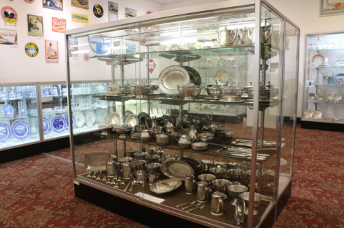 A glass display case filled with various silverware and serving dishes in a museum setting.
