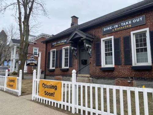 A brick building with signs for a café and ice cream shop, featuring a white picket fence and "Opening Soon" banners.