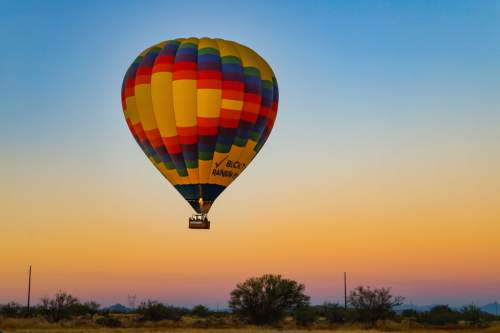 A colorful hot air balloon floats against a pastel sunset sky, with desert vegetation in the foreground.