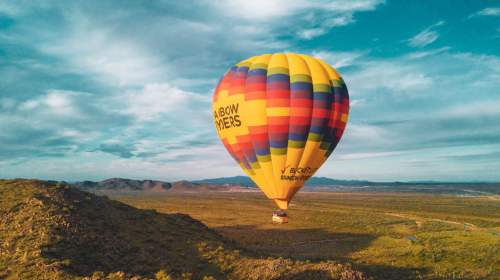 A colorful hot air balloon floats over a desert landscape under a blue sky with scattered clouds.