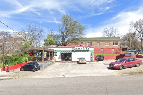 A small building with a sign reading "Ramalik's," surrounded by parked cars and trees under a blue sky.