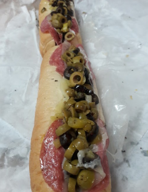A long sandwich filled with salami, olives, and green peppers on a white paper background.