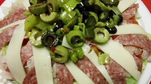 A colorful salad topped with sliced meats, cheese, and a mix of green and black olives.