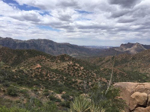 A panoramic view of rugged mountains and valleys under a cloudy sky, showcasing lush greenery and rocky terrain.