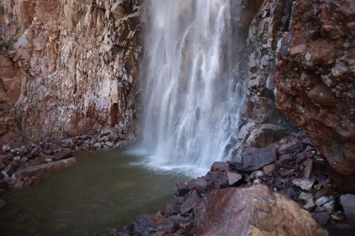A cascading waterfall flows into a rocky pool, surrounded by rugged cliffs and boulders.