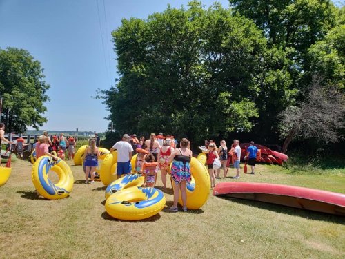 A group of people in swimsuits gather around yellow inflatable tubes on a sunny day near a river.