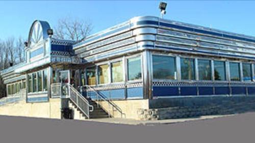 A retro-style diner with a blue and silver exterior, large windows, and a staircase leading to the entrance.