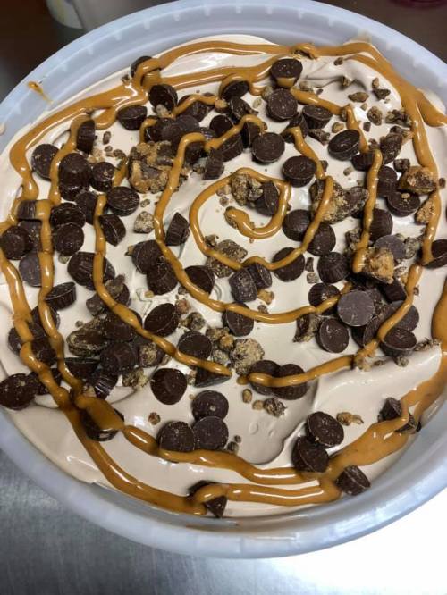 A creamy dessert topped with chocolate chips, crushed candy, and a swirl of peanut butter sauce.