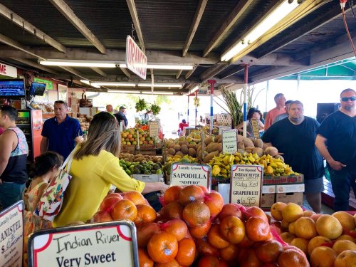 A bustling market scene with people shopping among colorful displays of fresh fruits and vegetables.